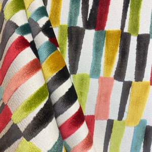 May include: A white fabric with a geometric pattern of colorful stripes. The stripes are in shades of red, green, yellow, blue, and pink. The fabric is folded in half, showing the pattern on both sides.