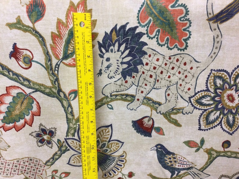 May include: A beige fabric featuring a multi-colored pattern of lions, birds, and floral motifs. A yellow ruler is placed vertically on the fabric, showing a measurement scale of 12 inches, indicating the scale of the printed design elements.