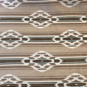 May include: A beige rug with a geometric pattern in shades of brown, white, and blue. The pattern features repeating diamond shapes with intricate details.