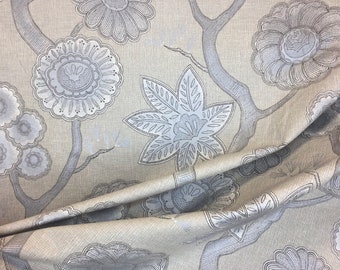 May include: A close-up of a beige fabric with a silver floral pattern. The fabric is folded and has a textured surface.