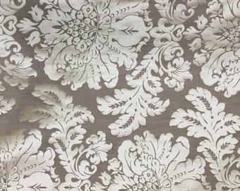 Peut inclure: Un gros plan sur un tissu beige avec un motif damassé blanc. Le tissu a un léger brillant et une texture douce.