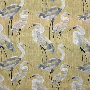 Pode incluir: Tecido com um padr&atilde;o repetido de gar&ccedil;as em aquarela em tons de cinza e branco sobre um fundo verde-oliva claro. As aves s&atilde;o retratadas com pesco&ccedil;os e pernas longas, criando um design inspirado na natureza.