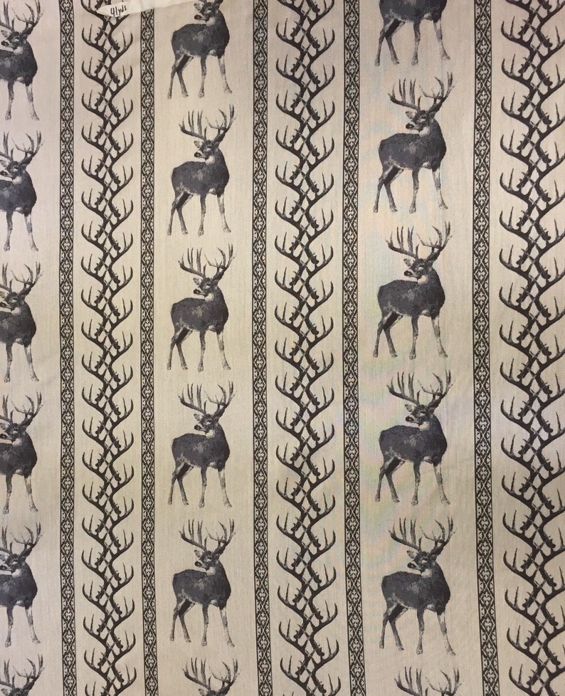 May include: A beige fabric with a repeating pattern of black deer silhouettes and stylized antlers. The deer are facing right and have large antlers. The background is a light beige color.