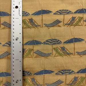 May include: Beige fabric with a repeating pattern of blue and green beach chairs and blue and white striped umbrellas. The fabric is textured and has a subtle sheen.