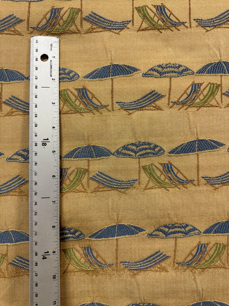 May include: Beige fabric with a repeating pattern of blue and green beach chairs and blue and white striped umbrellas. The fabric is textured and has a subtle sheen.