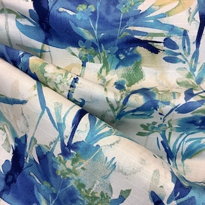 May include: Close-up of a fabric with a floral pattern. The design features blue, teal, and green watercolor-style flowers and foliage against a white background. The fabric is folded, showing the texture and depth of the material.