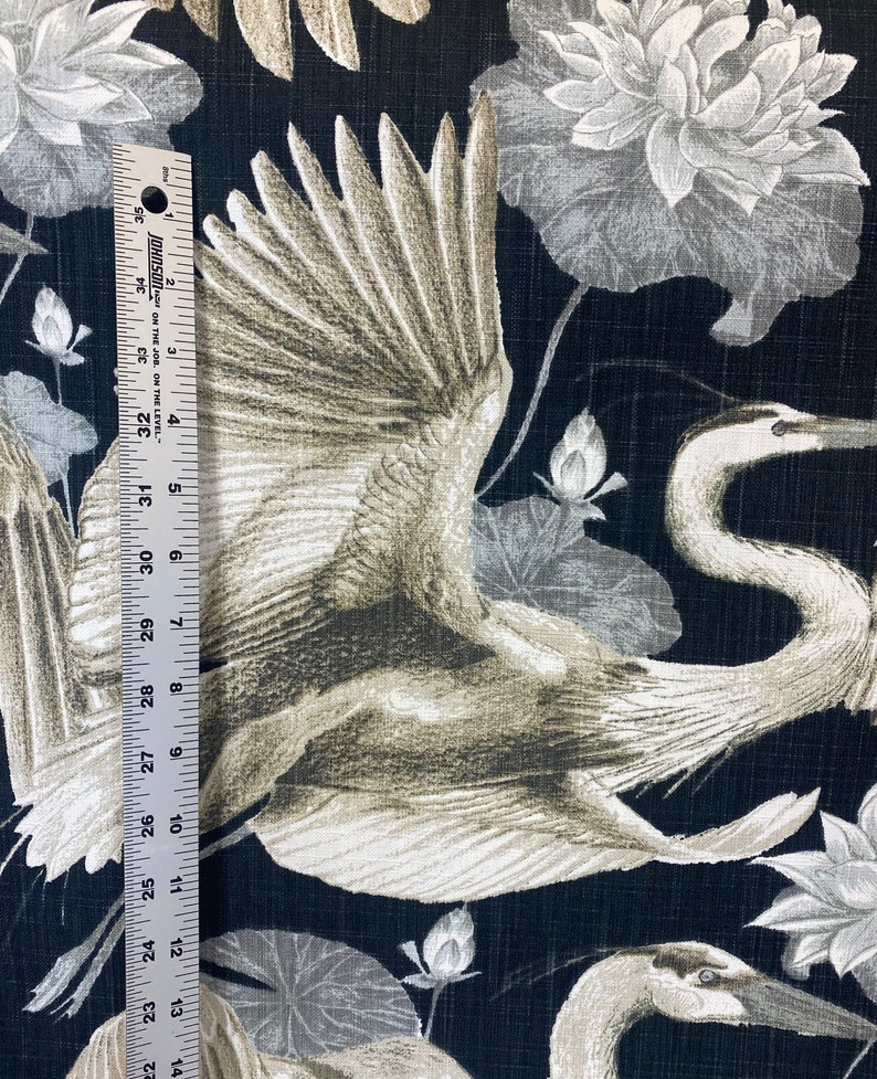 May include: Black fabric with a white and gray crane design. The crane is flying with its wings spread. The background is a dark black with a subtle texture. There are also white and gray lotus flowers in the background.