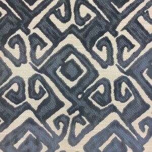May include: Close-up of a fabric with a repeating geometric pattern in shades of blue and gray. The design features stylized shapes with curved and angular elements, set against a neutral, textured background.