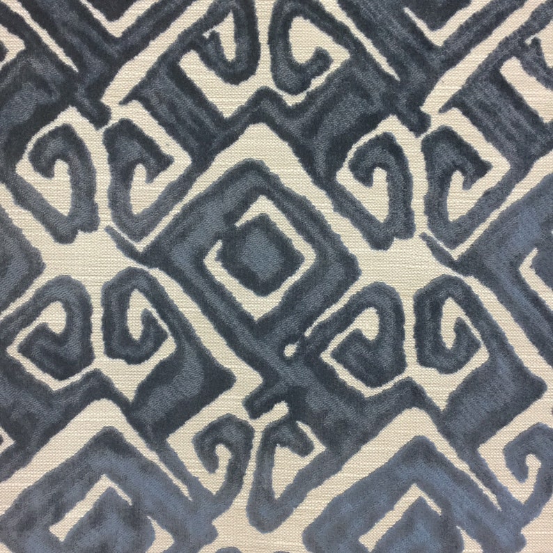 May include: Close-up of a fabric with a repeating geometric pattern in shades of blue and gray. The design features stylized shapes with curved and angular elements, set against a neutral, textured background.