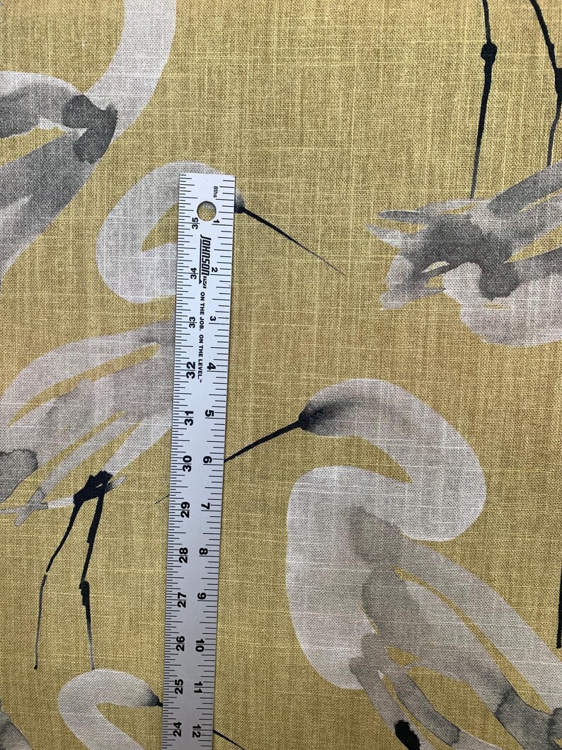 Pode incluir: Close-up de um tecido com um desenho de guindaste em aquarela em cinza e preto sobre um fundo amarelo dourado. Uma r&eacute;gua mostra as medidas em polegadas, cerca de 61-89 cm.