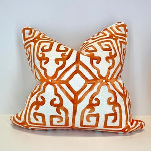 May include: A white pillow with an orange geometric pattern. The pattern is a repeating design of squares and lines.
