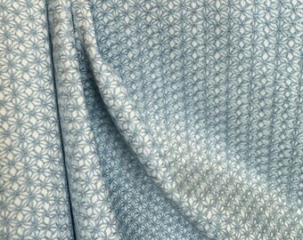 May include: A close-up of a light blue fabric with a white embroidered pattern of small flowers. The fabric has a subtle texture and a soft, drapey feel.