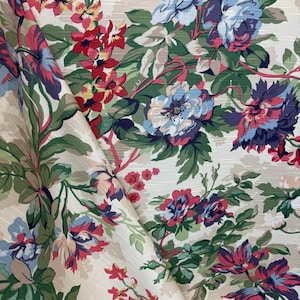 May include: A beige fabric with a floral pattern featuring red, blue, and white flowers. The fabric has a textured surface and a subtle sheen.