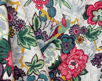 May include: A white fabric with a colorful floral pattern. The fabric features a variety of flowers, including pink, red, blue, and yellow flowers. There are also green leaves and a bird with a yellow beak.