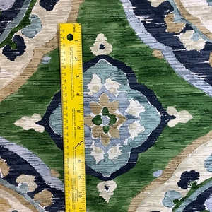 May include: A close-up of a fabric with a repeating pattern of blue, green, and beige. The fabric has a textured, brushed look. A yellow ruler is placed on the fabric to show the scale.
