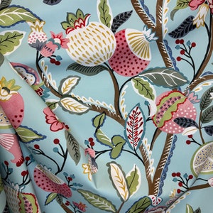 May include: A blue fabric with a repeating pattern of stylized green leaves, brown branches, and pink and white pomegranates.