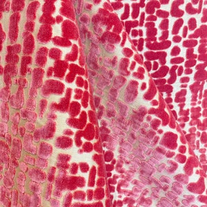 May include: A fabric featuring a raised, velvet-like texture in shades of deep pink and magenta, arranged in an irregular, abstract geometric pattern against a light beige, smooth background, creating a distinct contrast in both color and depth.
