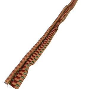 May include: A length of decorative trim with a woven pattern. The trim features alternating blocks of reddish-brown, green, and tan colours. The trim has a textured, ridged edge.