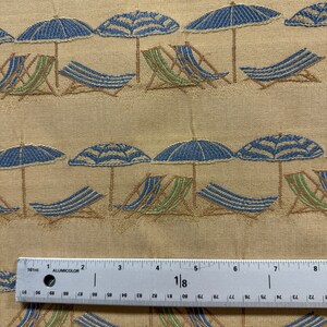 May include: Beige fabric with a repeating pattern of blue and green beach chairs under blue striped umbrellas. A ruler is in the bottom of the image.