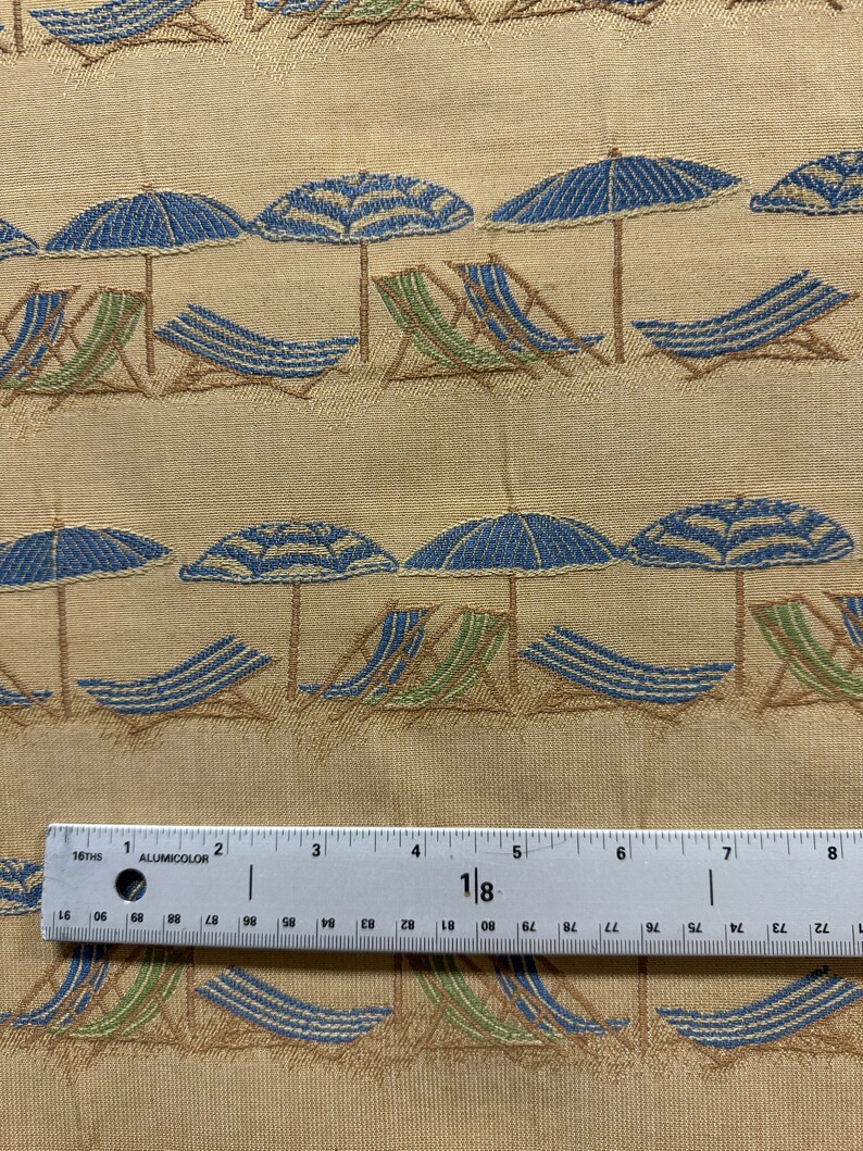 May include: Beige fabric with a repeating pattern of blue and green beach chairs under blue striped umbrellas. A ruler is in the bottom of the image.