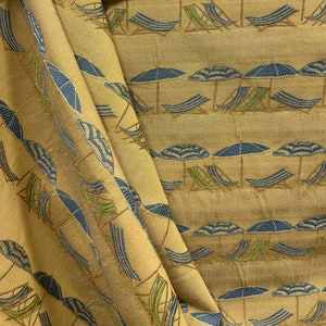 May include: A beige fabric with a repeating pattern of blue and green beach umbrellas and lounge chairs. The fabric has a woven texture.