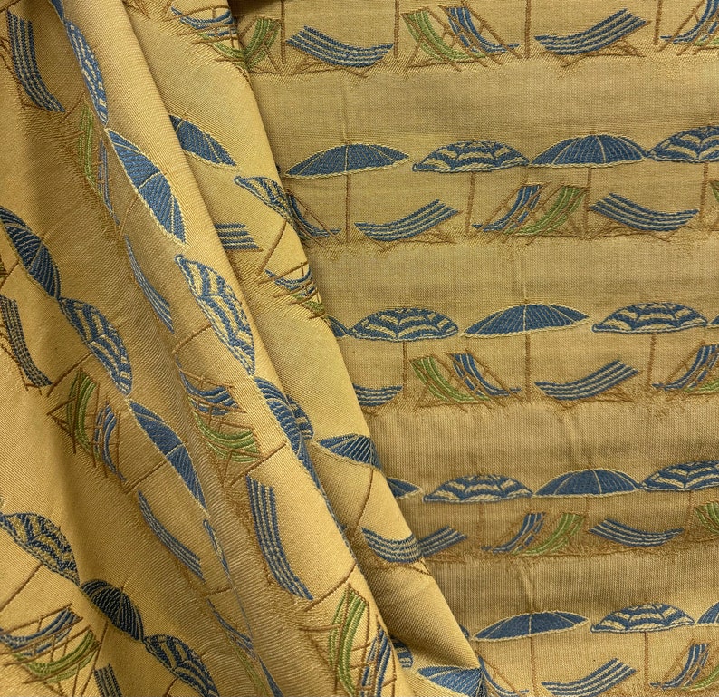 May include: A beige fabric with a repeating pattern of blue and green beach umbrellas and lounge chairs. The fabric has a woven texture.