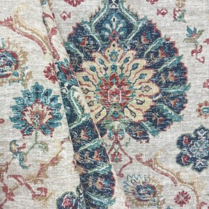 May include: A folded section of fabric with an intricate, vintage-style pattern. The design features large, ornate floral motifs in shades of navy blue, teal, red, and gold against a neutral, off-white background. The fabric has a textured appearance.