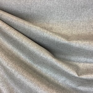 Peut inclure: Gros plan sur un tissu en herringbone argenté et gris avec un léger chatoiement. Le tissu a une surface texturée et un motif tissé.