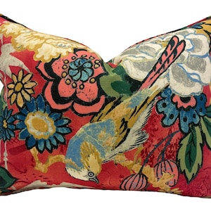 May include: A decorative rectangular pillow with a vibrant floral and bird pattern. The pillow features a red background with large flowers in shades of blue, yellow, and pink. A blue and yellow bird is prominently displayed, adding a touch of nature to the design.
