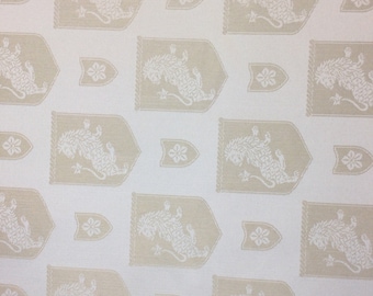 May include: White fabric with a repeating pattern of beige shields featuring a stylised lion design. The shields are surrounded by a rope-like border.