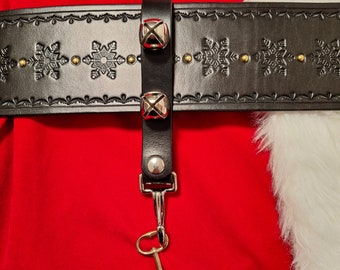 May include: A black leather belt with snowflake designs and a silver key attached to a loop with three silver bells. The belt is worn over a red and white Santa suit.
