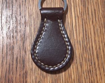 May include: A brown leather key fob with a silver metal ring. The fob has a stitched edge.