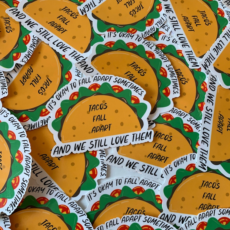 K&ouml;nnte beinhalten: Eine Sammlung bunter Aufkleber mit einem Cartoon-Taco mit dem Text "Tacos Fall Apart" und "And We Still Love Them". Die Aufkleber sind auf wei&szlig;em Papier gedruckt und haben eine gl&auml;nzende Oberfl&auml;che.
