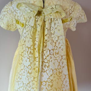 May include: A yellow lace dress with a large bow in the back. The dress has a fitted bodice and a full skirt.