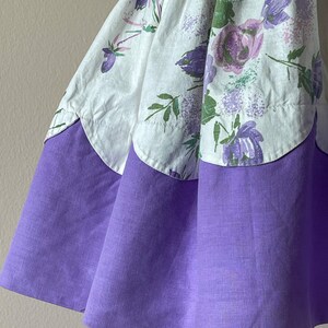 May include: A white and purple floral print skirt with a scalloped hem. The skirt has a solid purple bottom layer.
