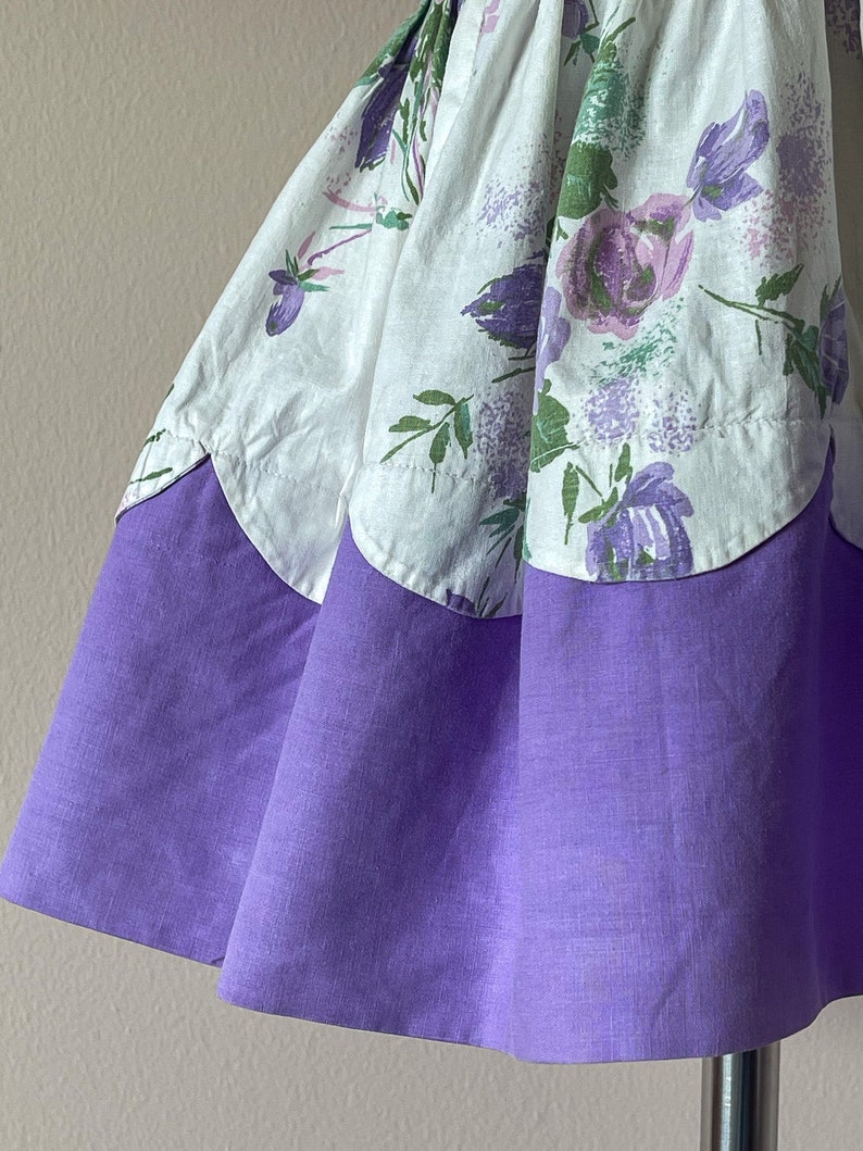 May include: A white and purple floral print skirt with a scalloped hem. The skirt has a solid purple bottom layer.