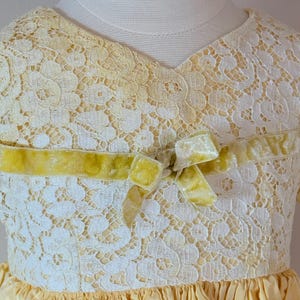 May include: A yellow lace dress with a velvet bow at the neckline. The dress has a ruffled skirt and is made of a soft, delicate fabric.