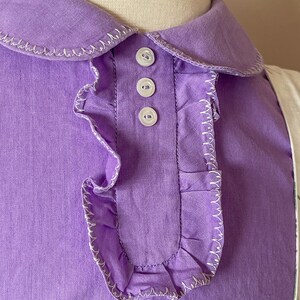 May include: A purple collared shirt with a ruffled trim and white buttons.