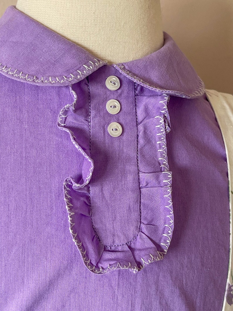May include: A purple collared shirt with a ruffled trim and white buttons.