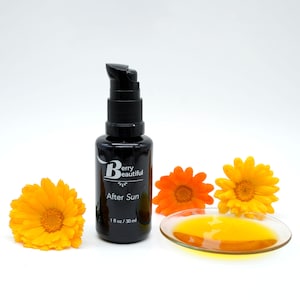 Berry Beautiful After Sun Serum in a Miron glass bottle with freshly picked golden and orange calendula flowers. A dish reveals the rich golden hue of calendula and vanilla-infused raspberry seed oil, crafted to soothe and hydrate sun-exposed skin