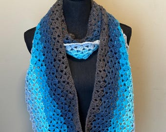 May include: A crocheted scarf with a gradient of blue and gray colors. The scarf is displayed on a black mannequin.