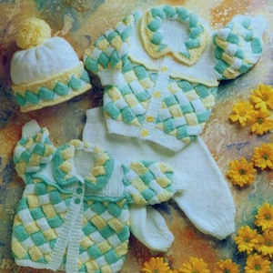 May include: A knitted baby outfit in white, yellow, and light green. The set includes a hat with a pom-pom, a cardigan, a pair of pants, and a pair of mittens. The cardigan and hat have a woven pattern design. Yellow flowers are scattered around the outfit.