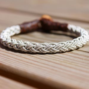 Può includere: Un braccialetto intrecciato in argento con chiusura in pelle marrone.