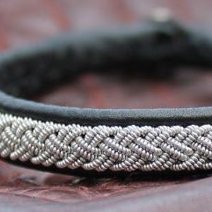 May include: A black leather bracelet with a silver braided design.