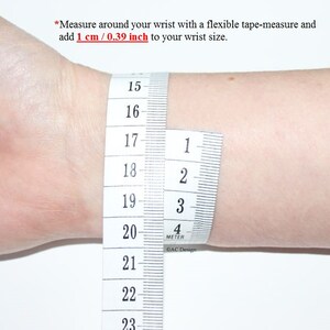 May include: A white tape measure wrapped around a wrist, showing measurements in inches and centimeters. The tape measure reads 15 to 23 inches and 1 to 4 centimeters. The text on the tape measure reads "4 METER" and "AC Design".