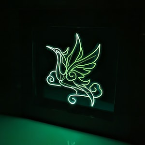 May include: A neon green hummingbird with stylised wings and clouds, framed in a black frame.