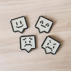 May include: Four white coasters with black outlines, each featuring a different pixelated emoji: a smiling face, a neutral face, a frowning face, and a surprised face.