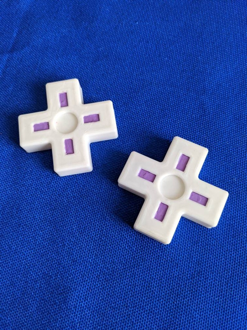 May include: Two white plastic plus signs with purple accents. The plus signs are on a blue background.