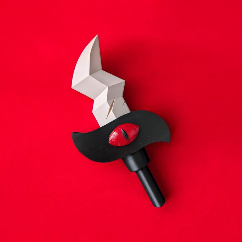 May include: A stylized sword with a white blade and a black handle and guard. The guard features a red eye design. The sword is set against a vibrant red background, creating a striking contrast.