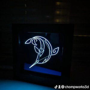 May include: A black framed light-up wall art piece with a white outline of a narwhal. The narwhal is facing left and has a long, thin horn. The background is black. The text "@chompworks3d" is visible in the bottom right corner.
